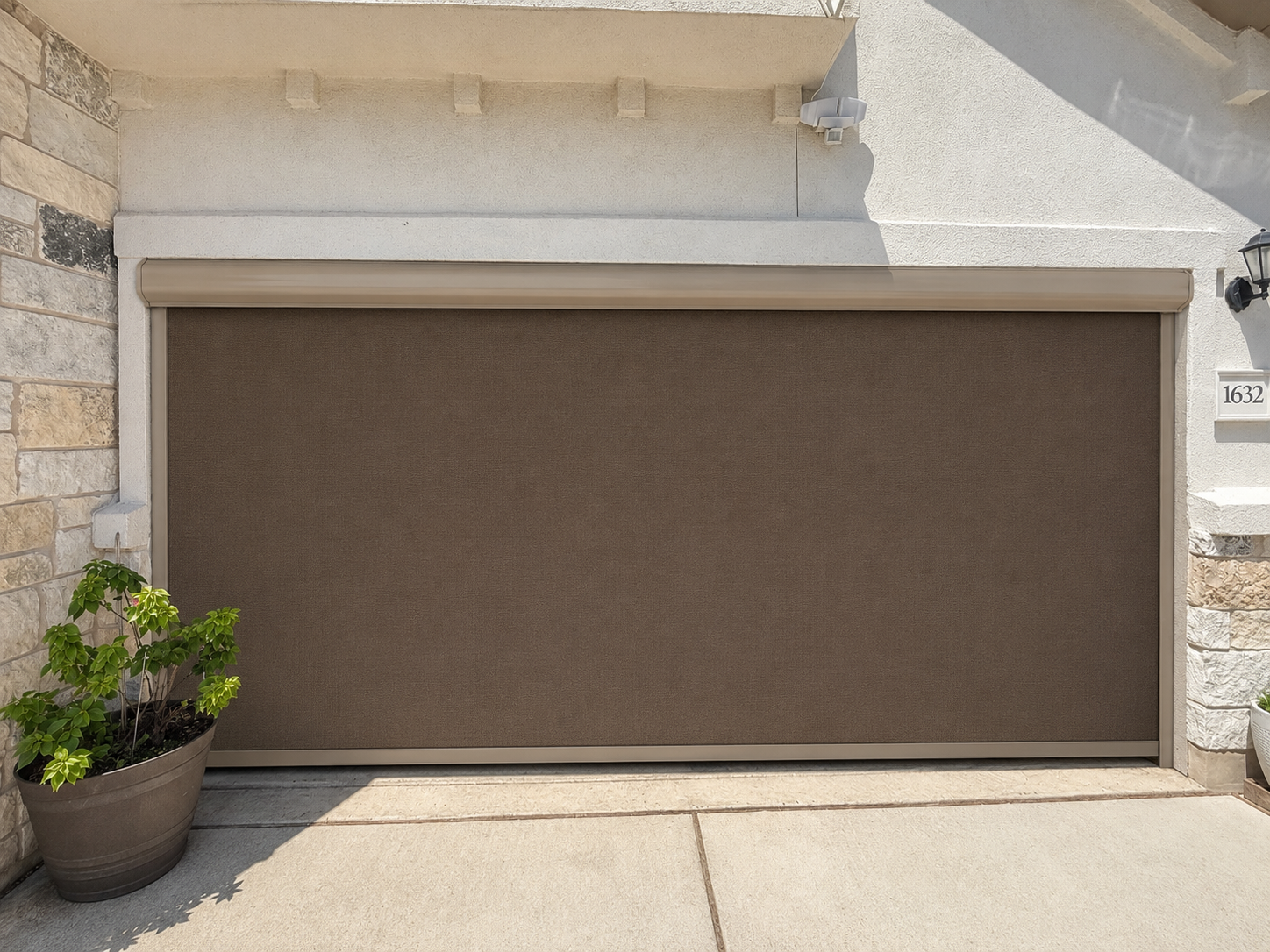 A bronze roller shade lowered across a wide patio opening on a stone and stucco home