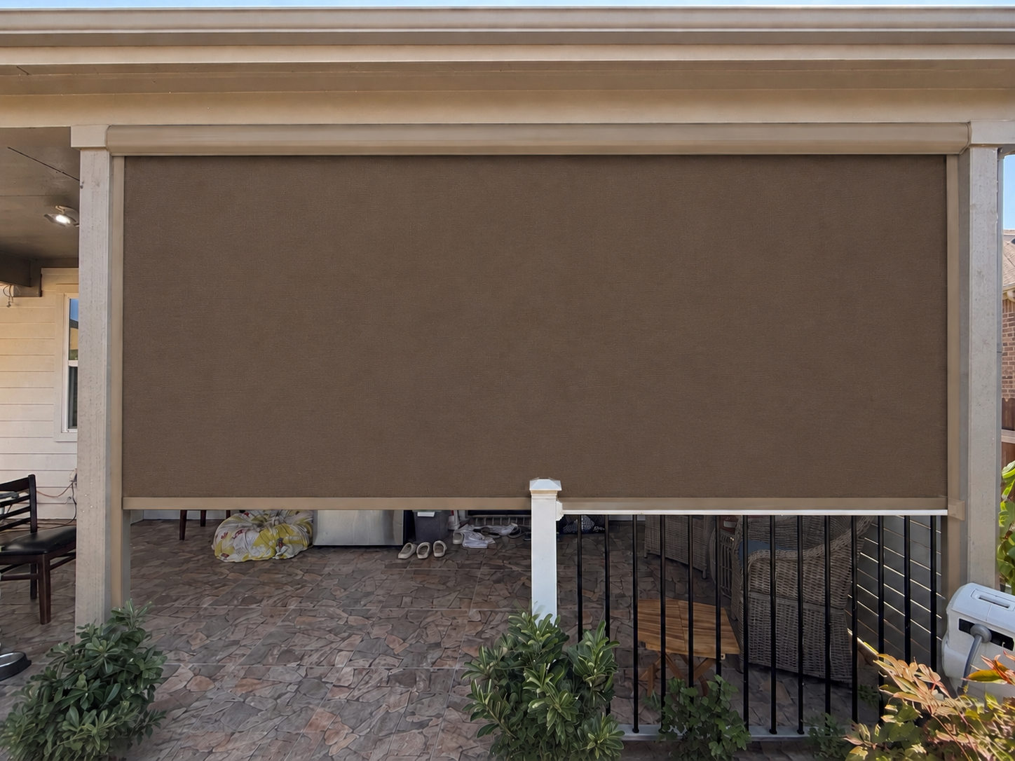 A patio shade lowered over a paver patio with seating and a metal railing