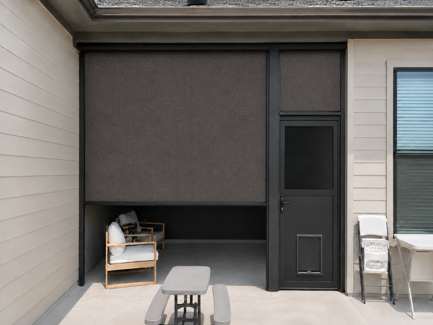 A dark roller shade lowered beside a screen door on a covered patio with seating