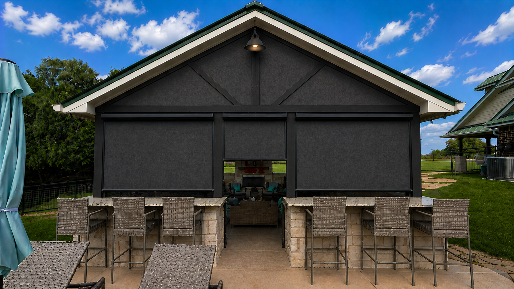 A covered patio and outdoor kitchen enclosed by dark motorized shades under a blue Texas sky