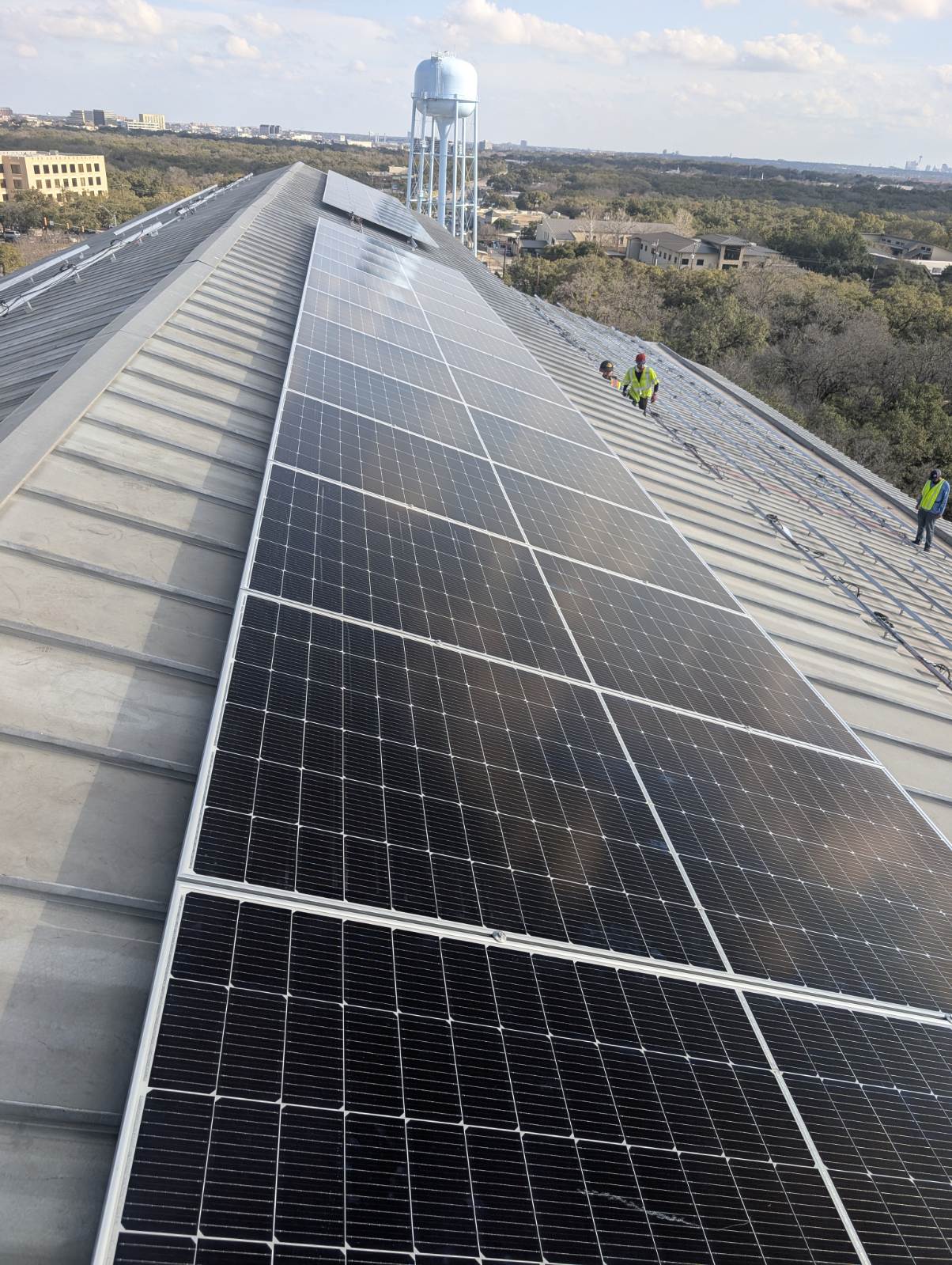 Crew installing a commercial solar array on a standing-seam metal roof